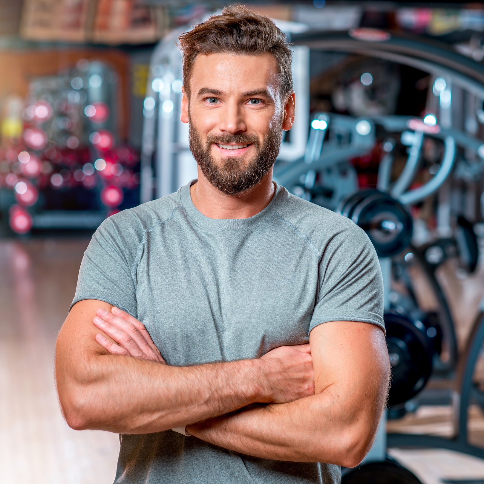 Smiling man with a fit physique standing in a gym, representing fitness.